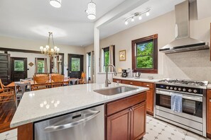 A modern kitchen with a central island, stainless steel appliances, and a dining area with wooden chairs. - Historic charm in downtown Tryon; 18 Minutes from Tryon Intl Equestrian Center (Tryon)