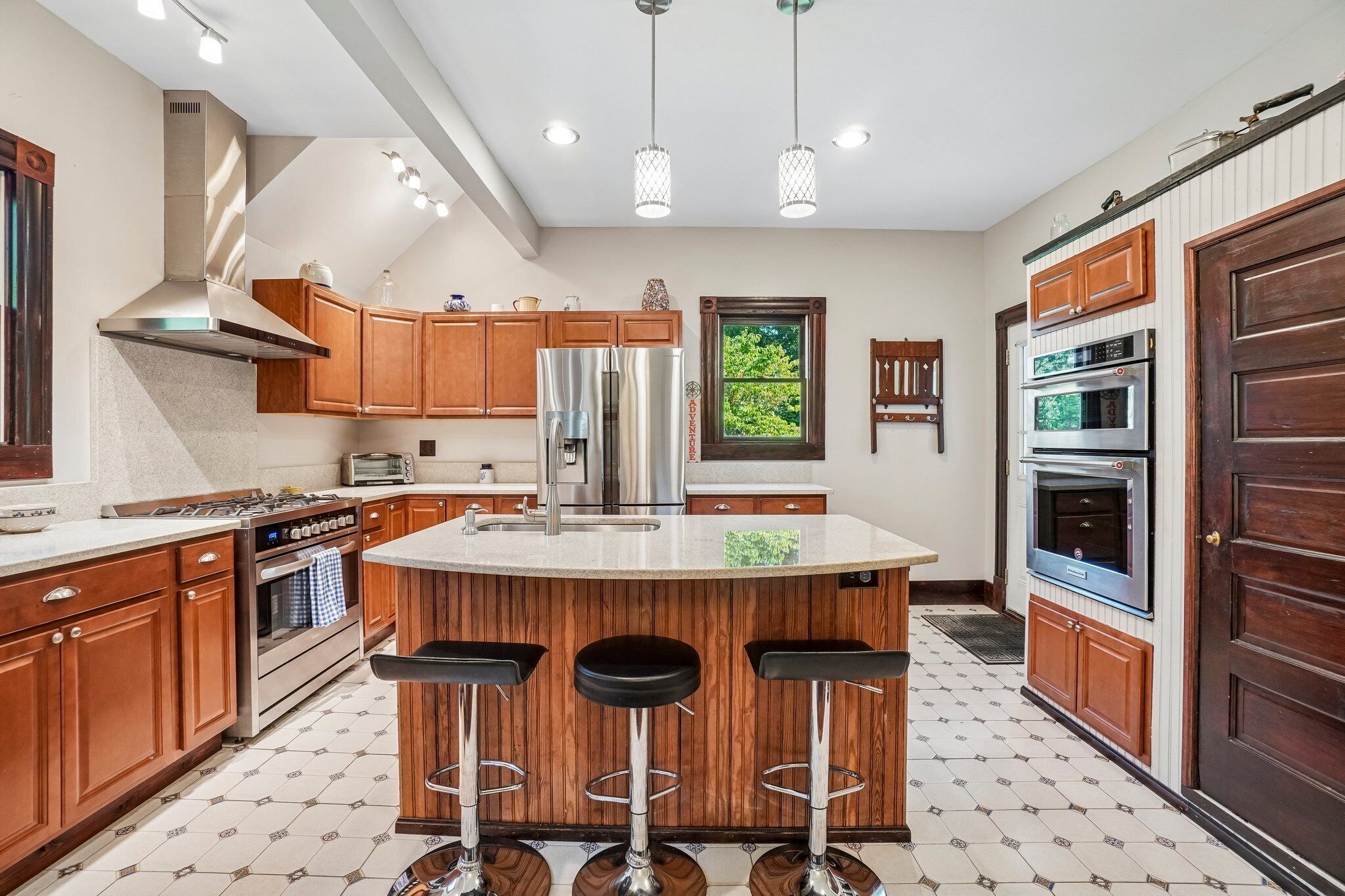 A modern kitchen with a central island, stainless steel appliances, wooden cabinets, and a large window.