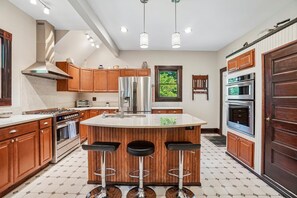 A modern kitchen with a central island, stainless steel appliances, wooden cabinets, and a large window. - Historic charm in downtown Tryon; 18 Minutes from Tryon Intl Equestrian Center (Tryon)