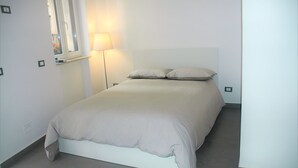 Una cama bien tendida con cabecera, una lámpara de noche y una ventana con vistas al exterior.