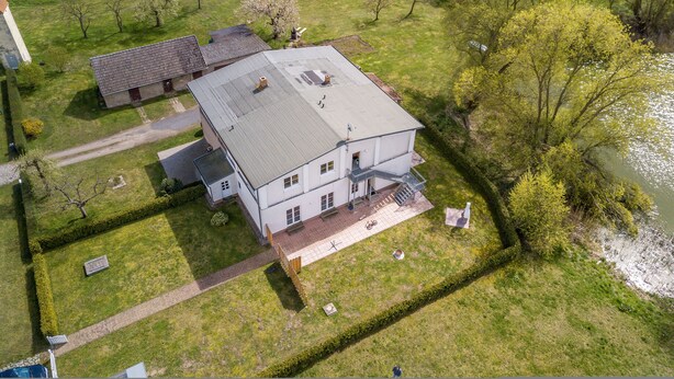 Ovenfra ses et stort, etetages hus med skrå tag, en veranda og en trappe, der fører til en indgang på første sal.