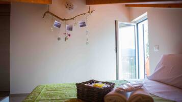 Una camera d'hotel con un letto, una coperta verde fantasia, un cesto di vimini con asciugamani e una decorazione a parete con fotografie e ornamenti appesi.