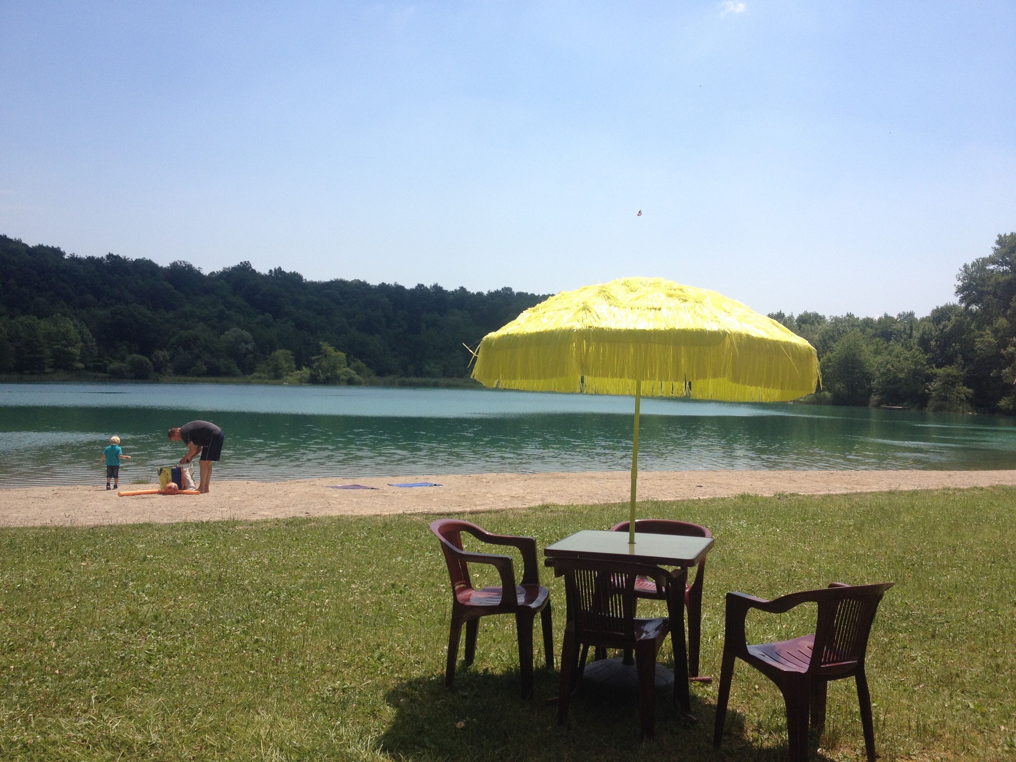 A lakeside setting with a yellow umbrella, a table, and chairs.