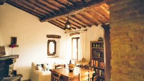 A rustic room with exposed wooden beams, a wooden dining table, a white sofa, and a bookshelf.
