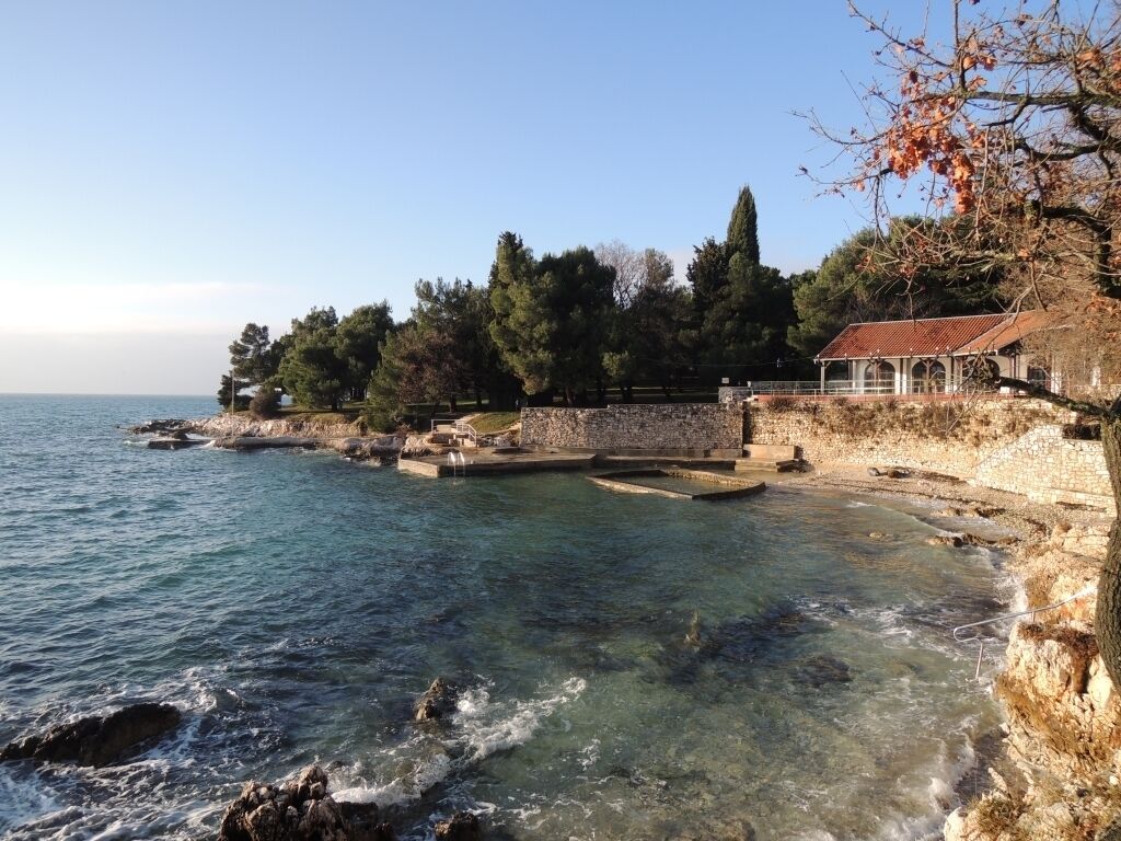A coastal property with a stone wall, a small building with a tiled roof, and a clear view of the sea.