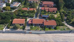 An aerial view of a coastal property with multiple buildings, a beach, and clear turquoise waters. - Deluxe three-room apartments - at Le Casette sul Mare (Capo Vaticano)