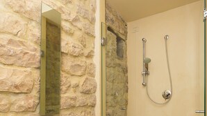 A bathroom with a stone wall, a white sink, a mirror, and a walk-in shower.