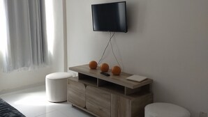 Ett modernt sovrum med en säng, en byrå i trä, en tv som är monterad på väggen och ett fönster med gardiner.