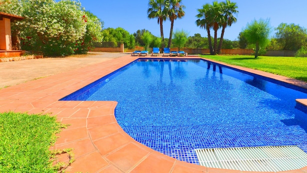 A swimming pool with blue tiles, surrounded by a brick patio and green grass. - Can Toni, Wi-fi, Pool, Garden, 15 Minutes From the beach Es Trenc  (Mallorca)