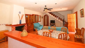 A dining area with a wooden table and chairs, a kitchen with a brick fireplace, and a staircase leading to another level. - Can Toni, Wi-fi, Pool, Garden, 15 Minutes From the beach Es Trenc  (Mallorca)