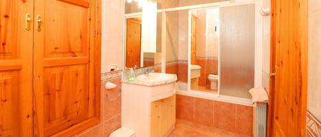 A bathroom with wooden cabinets, a sink, a toilet, and a shower area.