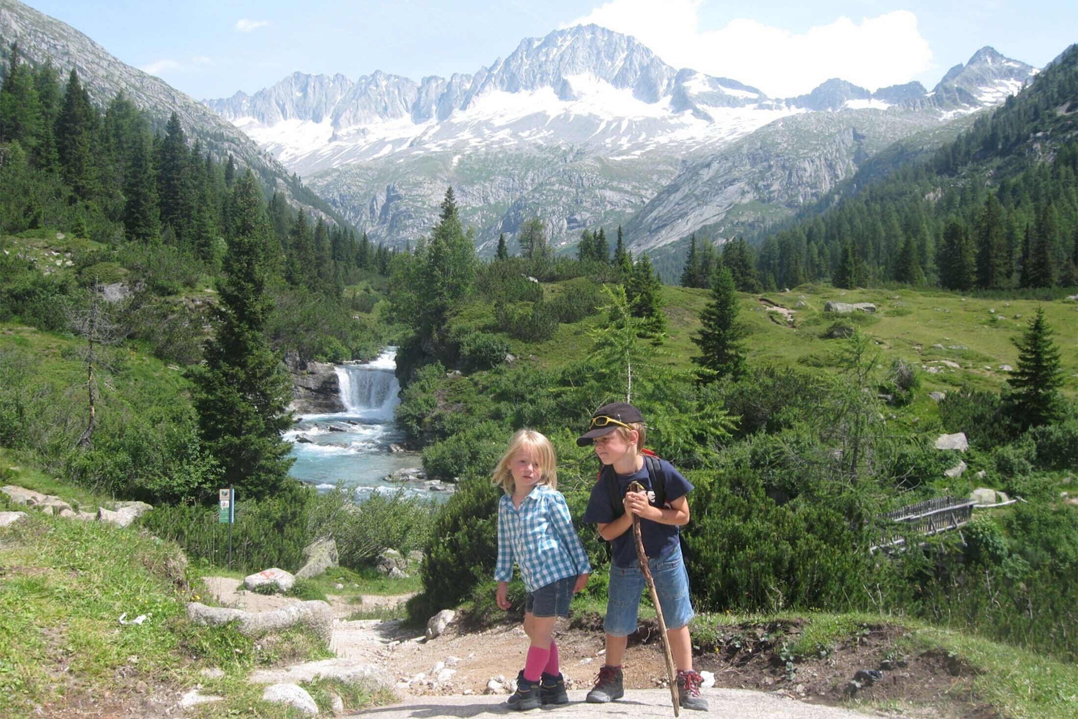 A mountainous landscape with a waterfall, dense forest, and rocky terrain.