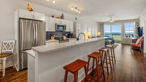 A modern kitchen with a central island, stainless steel appliances, and a view to the outside. - SC303 Seaside Dream by First Flight Rentals (Kill Devil Hills)