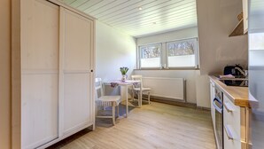 Eine Küche mit Holzboden, einem Tisch mit Stühlen, einem Heizkörper und einem Fenster mit Jalousien.