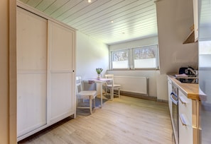 Eine Küche mit Holzboden, einem Tisch mit Stühlen, einem Heizkörper und einem Fenster mit Jalousien.