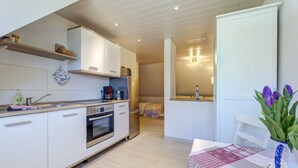 Eine kleine Küche mit weißen Schränken, einem Edelstahlkühlschrank und einem eingebauten Backofen.