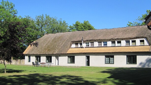 Ein traditionelles Gebäude mit Strohdach, schlichter Fassade und einer Reihe von Fenstern.
