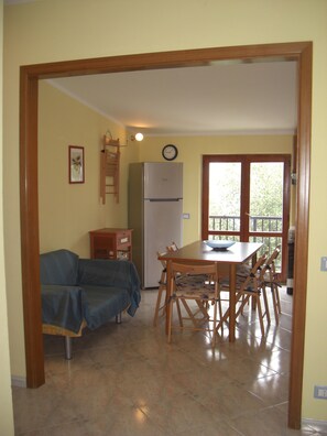A dining area with a wooden table and chairs, a refrigerator, and a clock on the wall.