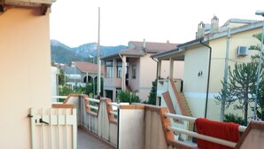 A tiled patio area with a railing, a red bench, and a view of neighboring buildings. - House 2 rooms +Garden, barbecue, children max 11 years free, in Costa Verde.  (Fluminimaggiore)