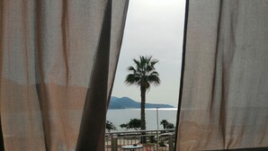 A view through sheer curtains of a balcony with a palm tree and a distant body of water. - House 2 rooms +Garden, barbecue, children max 11 years free, in Costa Verde.  (Fluminimaggiore)