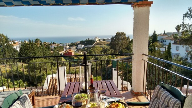 Un balcón con una mesa dispuesta para una comida, con vistas a un pueblo costero.