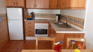 Cocina compacta con armarios de madera, un refrigerador blanco, un horno y un lavamanos.