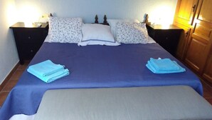 Una cama bien hecha con una colcha azul y blanca, dos almohadas y una manta azul a juego doblada sobre la cama.