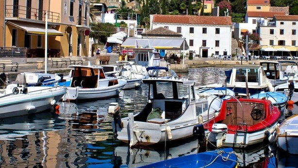 Uma marina com vários barcos atracados, cercada por edifícios com sacadas e uma colina ao fundo.