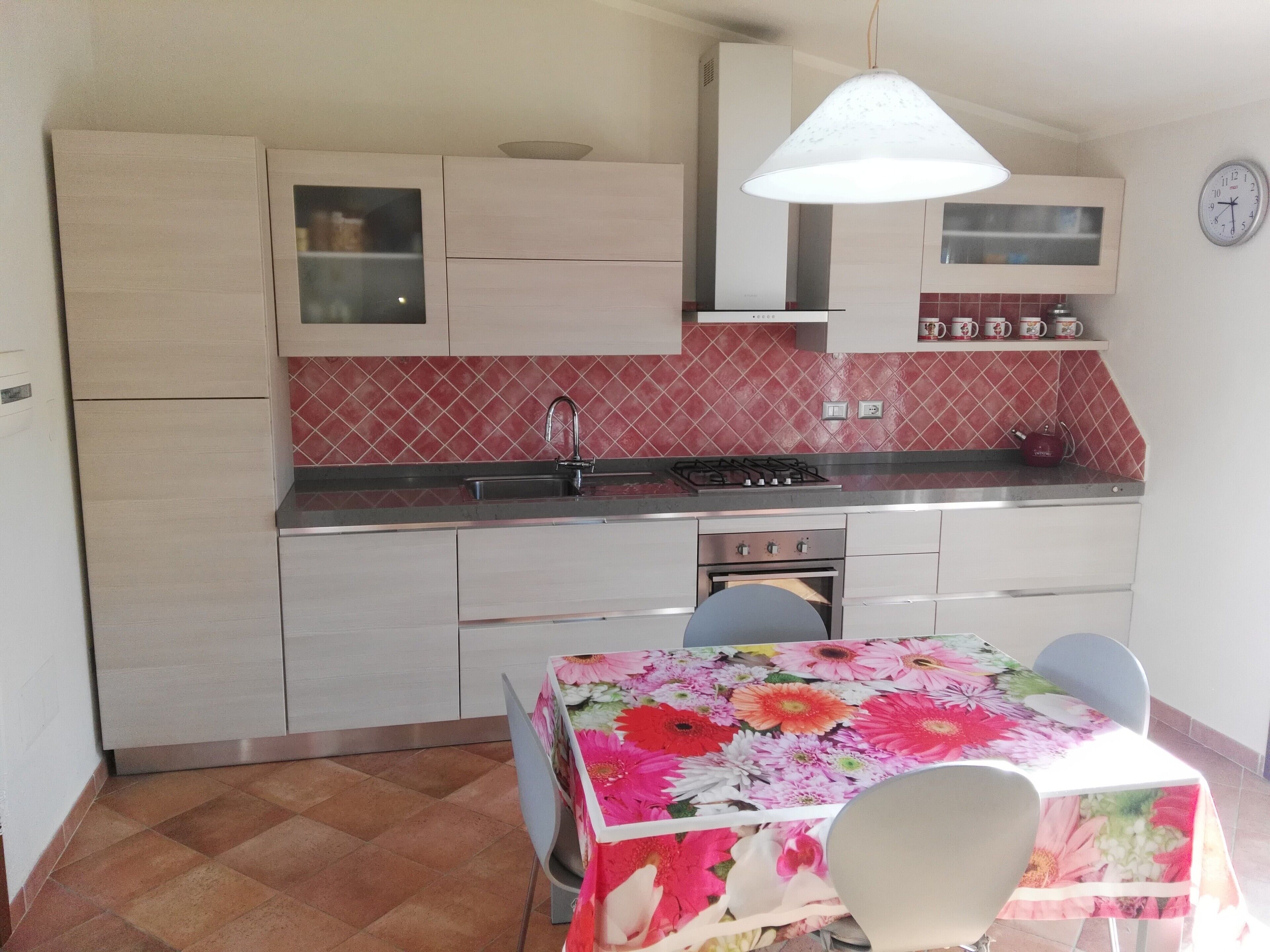 A compact kitchen with a sink, stove, and oven. There is a dining table with chairs and a floral tablecloth.
