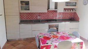 Une cuisine compacte équipée d’un évier, d’une cuisinière et d’un four. On y trouve une table à manger avec des chaises et une nappe à motifs floraux.