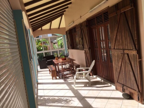 A covered patio area with a table and chairs, a view of the outdoors, and wooden doors.