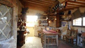 Een landelijke keuken met houten balken, een tafel met stoelen en verschillende keukengerei en flessen.