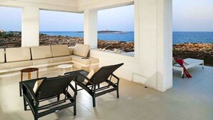 Ein modernes Wohnzimmer mit einem großen Fenster mit Blick auf einen felsigen Strand und das Meer.