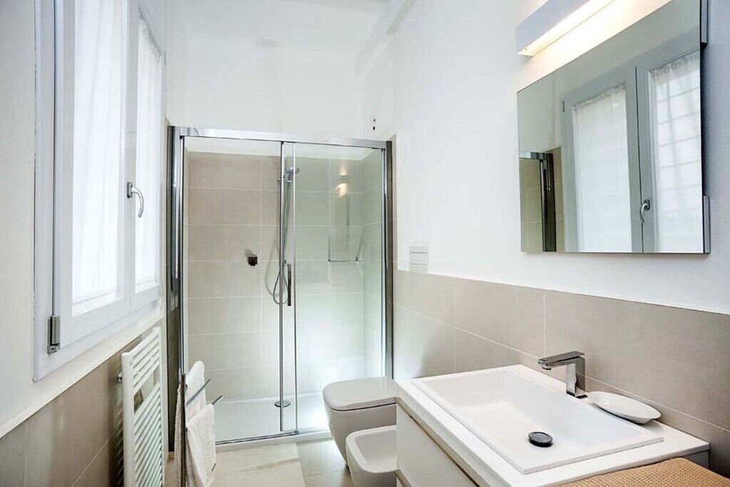 Een moderne badkamer met een douchecabine van glas, een witte wastafel met één kom en een grote spiegel boven de wastafel.