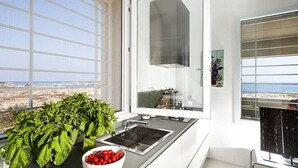 Eine moderne Küche mit einem großen Fenster mit Blick auf einen Strand, einem Spülbecken und einer Schüssel mit Tomaten.