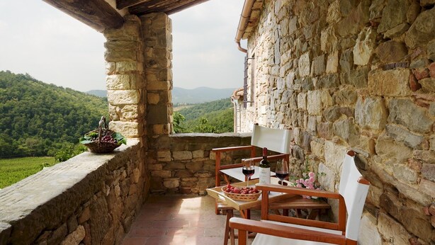 Un balcon en pierre, agrémenté d’une table et de chaises, qui offre une vue sur une vallée verdoyante.