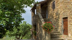 Un bâtiment en pierre avec un escalier en bois menant à une porte, le tout entouré de verdure.