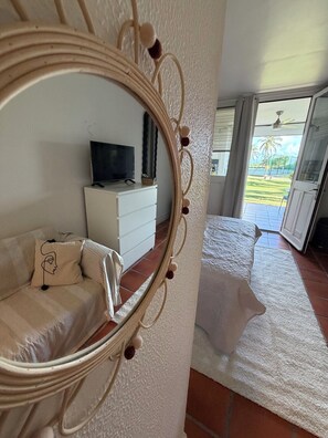 Ein Zimmer mit einem Bett, einer weißen Kommode, einem Fernseher und einem großen Spiegel mit Verzierungen.