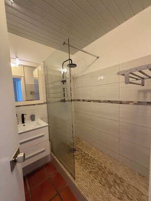 Ein modernes Badezimmer mit Duschkabine aus Glas, einem weißen Waschbecken mit Spiegel und gefliesten Wänden.