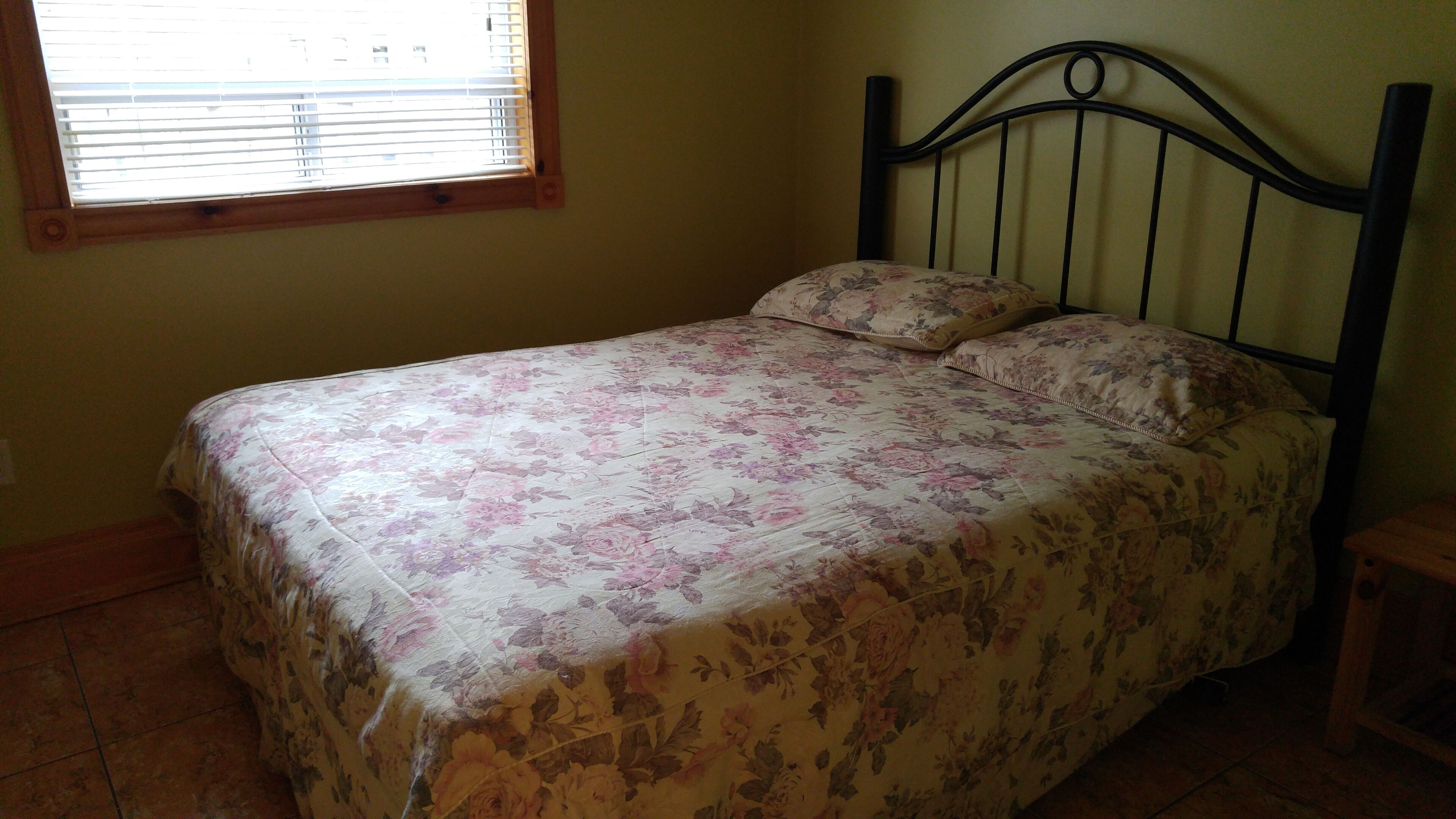 A bed with a floral bedspread and a matching pillow in a room with a window and a wooden headboard.