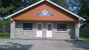 A two-story building with a stone facade, a wooden gable roof, and a sign indicating it is a Suites of Vasaga with weekly rentals. - Suites of Wasaga - Beach Area 1 (Wasaga Beach)