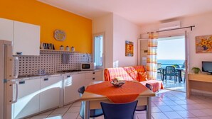 A kitchen with white cabinets, a microwave, and a dining area with a table and chairs. - Apartment Lumia Standard (Sciacca)