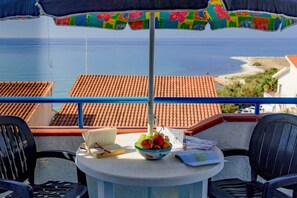 A balcony with a table, chairs, a bowl of fruit, a book, and an umbrella. - Apartment Lumia Standard (Sciacca)