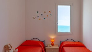 A room with two beds, a nightstand with a lamp, a window with a view of the sea, and a wall with butterfly decals. - Apartment Lumia Standard (Sciacca)