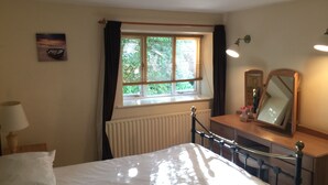 Un dormitorio con cama, cómoda, espejo, ventana con cortinas, radiador y lámpara.