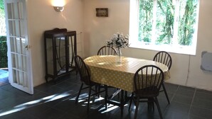 Comedor con una mesa dispuesta para cuatro, un jarrón de flores y una ventana con vistas a árboles.