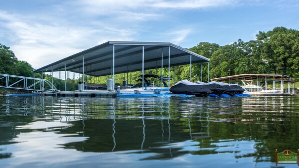 A covered boat dock with a metal frame and a roof, surrounded by calm water and greenery. - Home On Private Waterfront Resort with Pool Access and Dock Slip Access (Grove)