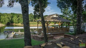 A gazebo with a roof and wooden railings, situated by a lake with a dock and boats. - Home On Private Waterfront Resort with Pool Access and Dock Slip Access (Grove)