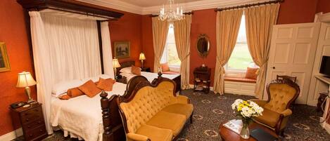 A hotel room with a bed, a sofa, a chair, a small table with a vase of flowers, and a television.