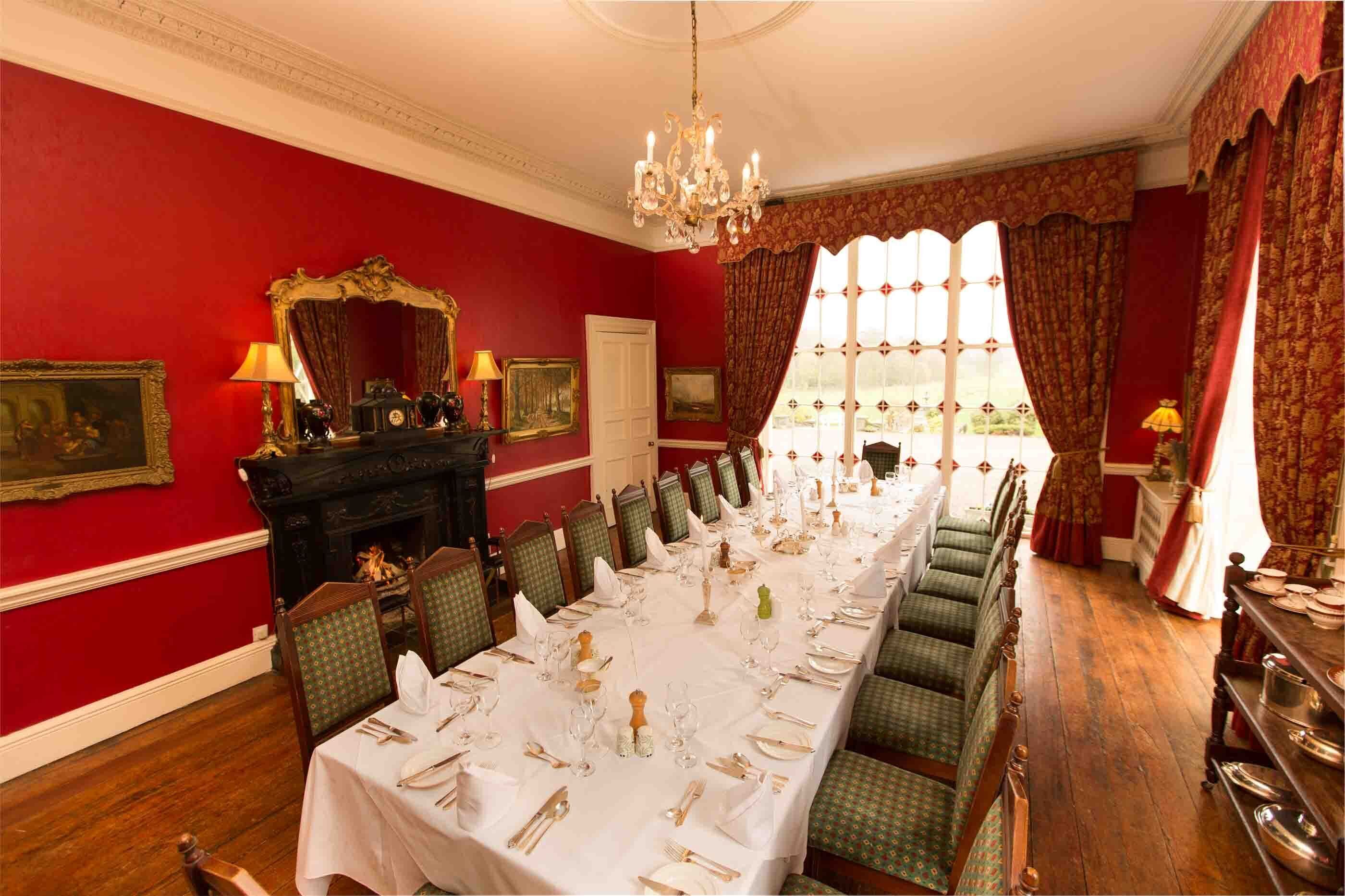 Une salle à manger élégante, avec une longue table dressée pour un repas, des murs rouges et un lustre.